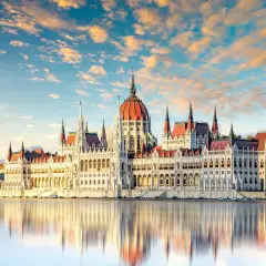 Budapeszt: Parlament odbija się w wodzie przy zachodzącym słońcu. Ceny noclegów i atrakcji są tu przystępne.