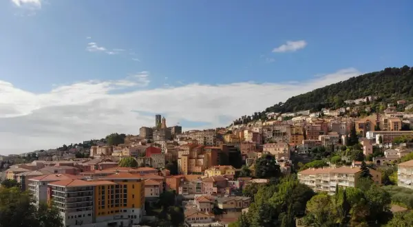 Widok na miasteczko na wzgórzu, z kolorowymi budynkami i zielenią, przypominający scenerię z festiwalu Cannes.