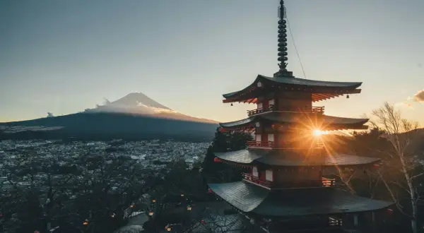 Zachód słońca nad Japonią. Góra Fudżi w chmurach, a przed nią pagoda rozświetlona promieniami słońca. Piękna pogoda.