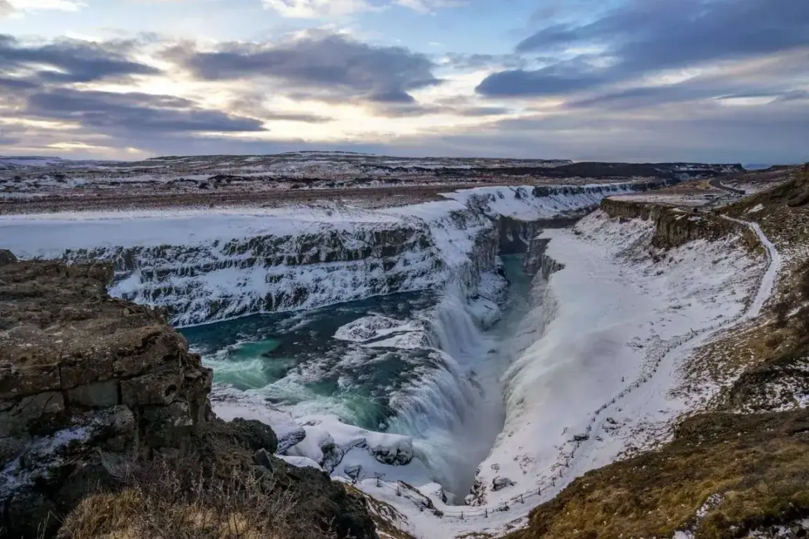 Potężny wodospad Gullfoss, część Złotego Kręgu Islandii, w zimowej scenerii. Woda spływa kaskadami do kanionu, otoczonego śniegiem i lodem.