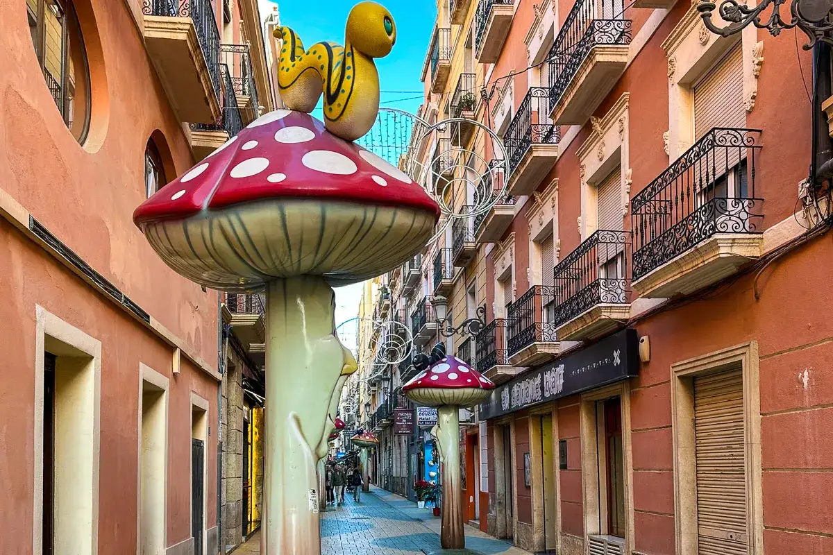 Alicante stare miasto ozdobione bajkowymi grzybami i gąsienicą. Wąska uliczka z kamienicami i balkonami.