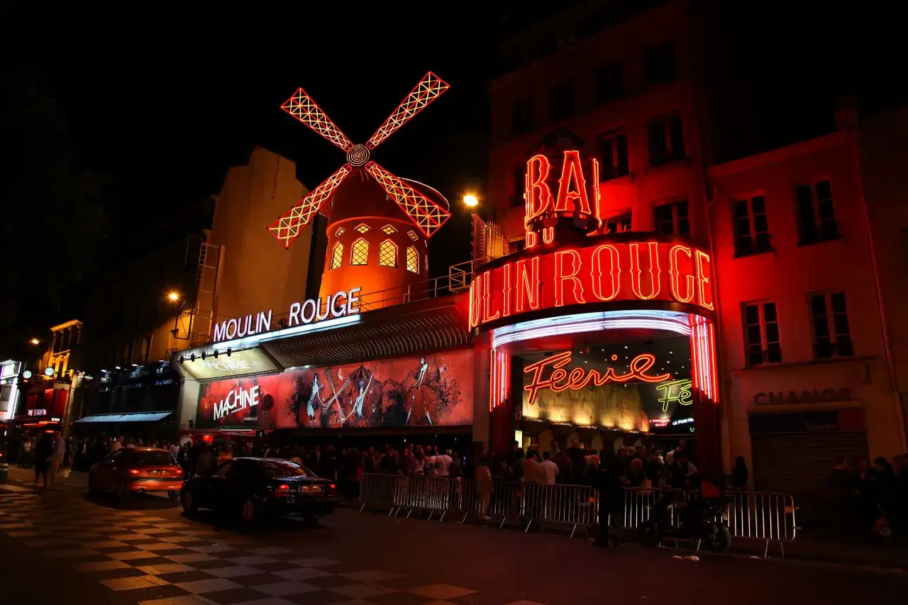 Nocny Paryż rozświetlony neonami Moulin Rouge. Słynny czerwony wiatrak i wejście do kabaretu przyciągają tłumy.