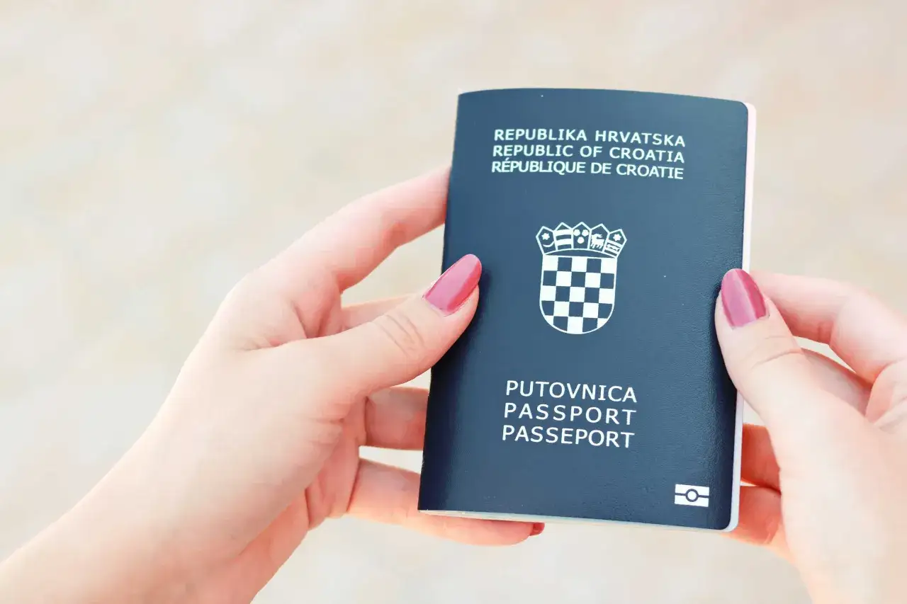 Dwie dłonie trzymają granatowy paszport Republiki Chorwacji. Czy to dowód czy paszport? To paszport, niezbędny do podróży.