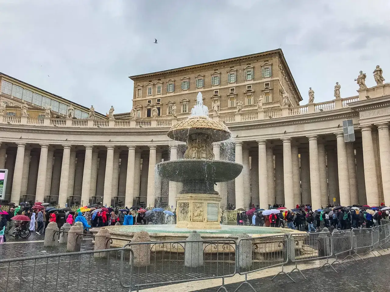 Tłum turystów z parasolami podziwia fontannę przed pałacem papieskim w Rzymie.