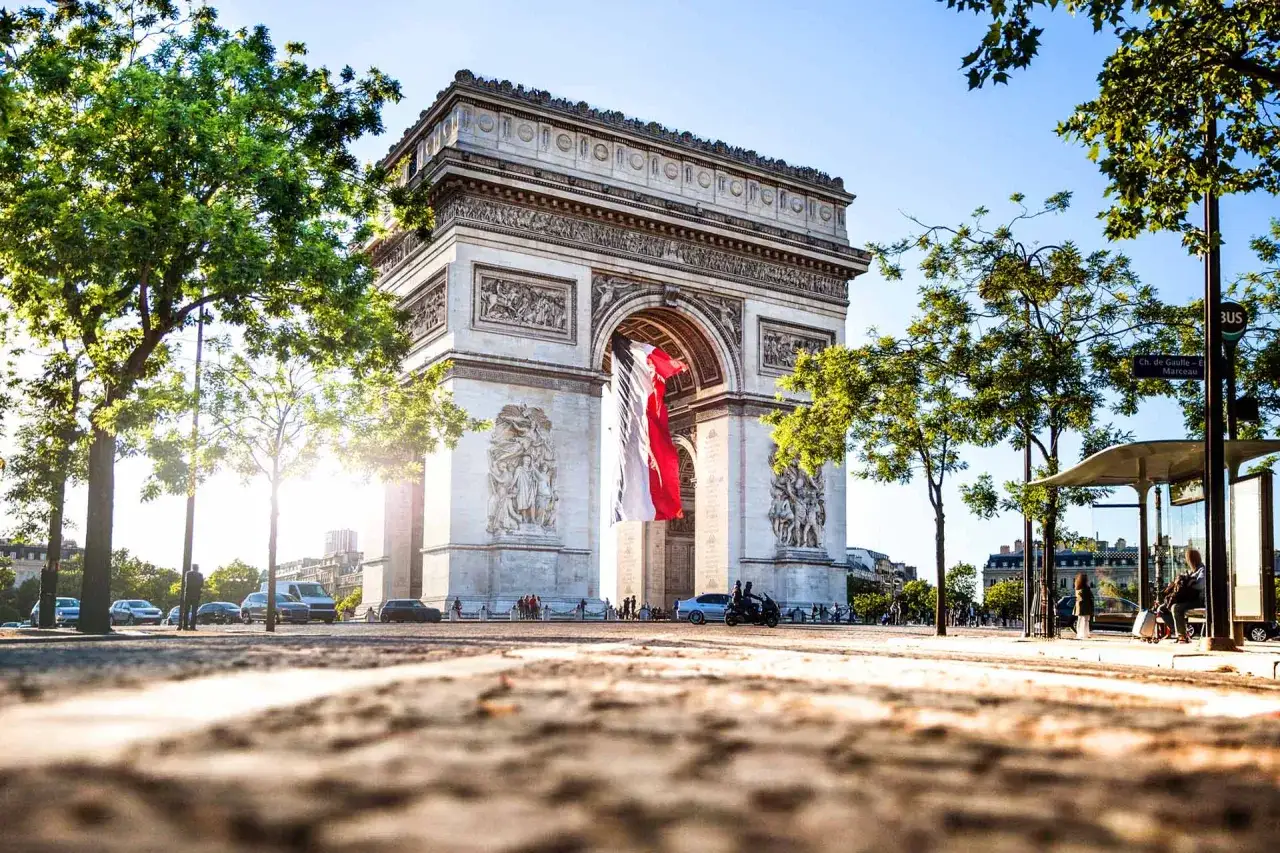 Łuk Triumfalny na Champs-Élysées, ozdobiony francuską flagą, w słoneczny dzień.