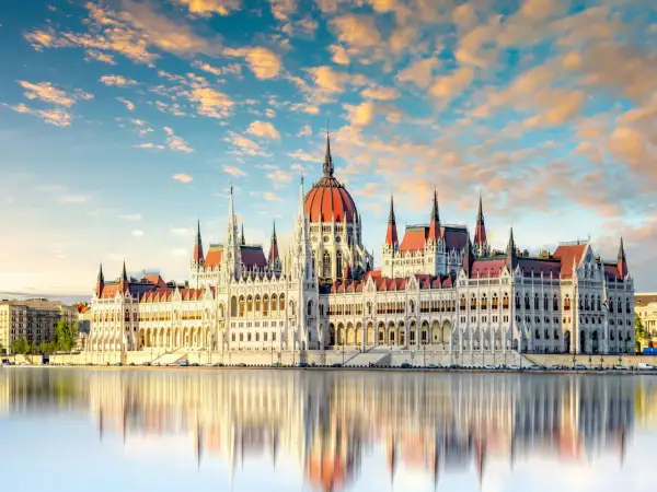 Budapeszt: Parlament odbija się w wodzie przy zachodzącym słońcu. Ceny noclegów i atrakcji są tu przystępne.